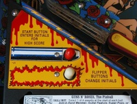 Image # 33086: Guns N' Roses Sample Game - Left Apron Sticker 
(On production games, the words 'Shoot Again' are printed to the left of the red bulb, and 'Magnets On' to the left of the white bulb. Game has serial number 110878 manufactured May 23, 1994.)
