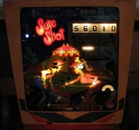 Image # 43138: Sure Shot Illuminated Backglass 
(The 100,000 point score is illuminated. An operator's sticker is affixed to the lower right corner of the glass.)