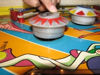Image # 59679: Carnival Pop Bumper Activation 
(The pop bumper is manually operated to simulate a ball hitting it from the direction of the photographer's camera. A nearby pop bumper is in normal position. Serial number 0400.)